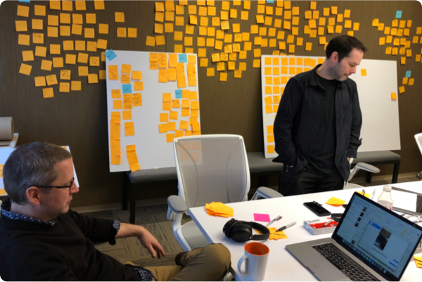 Two men collaborating to organize the collected data points. The wall behing them is covered in individual post-it notes